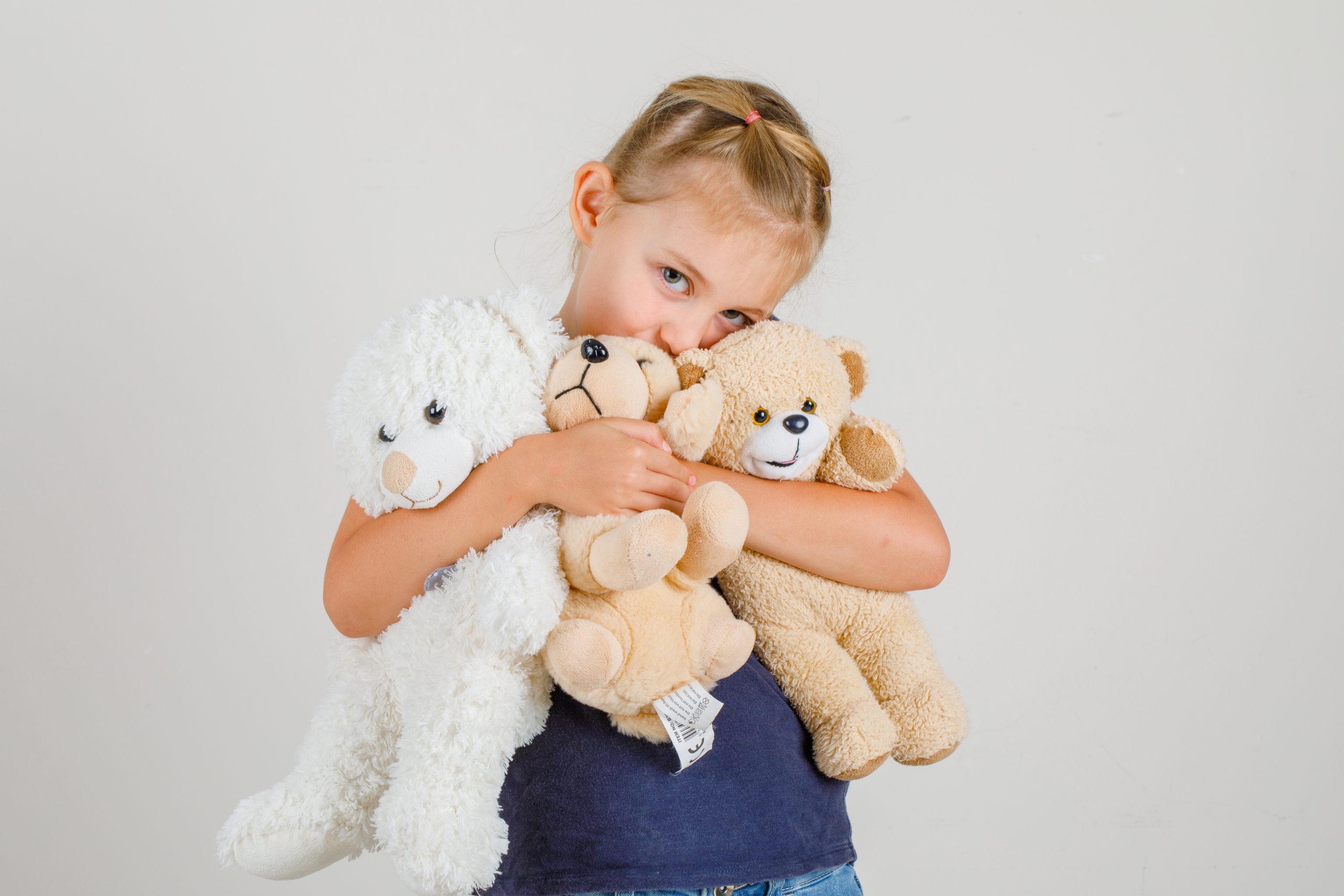 mainan boneka organik - Little girl hugging teddy bears and smiling in t-shirt and denim skirt , front view.
